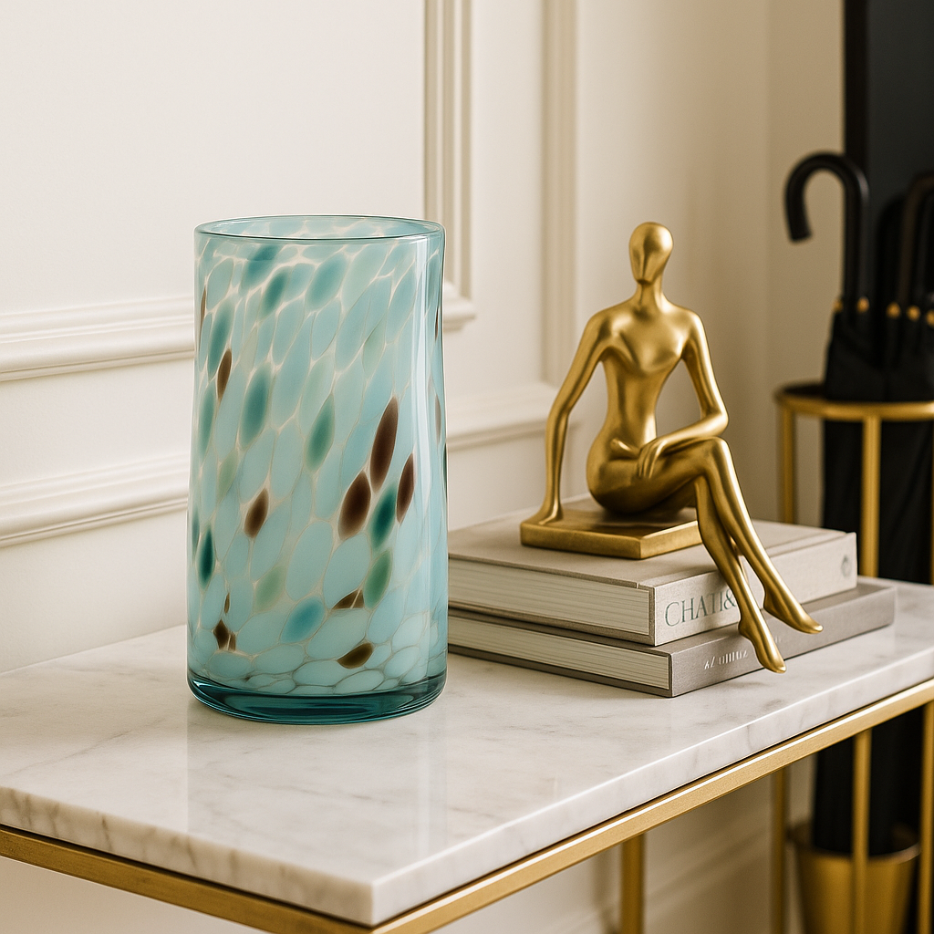 Hand-blown turquoise marbled glass vase on marble console with gold statue and umbrella stand.