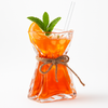Folded Glass Cocktail Vase filled with an orange cocktail, garnished with fresh mint and citrus, styled on a white background.