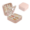 Open blush pink travel jewelry organizer with compartments holding colorful rings and earrings.
