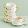 Stacked white porcelain teacups with gold rims and handles beside filled teacup on saucer, Fable & Feather Home branding.